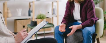 Therapist listening and taking notes while a client speaks, reflecting the human connection strengthened through better documentation.